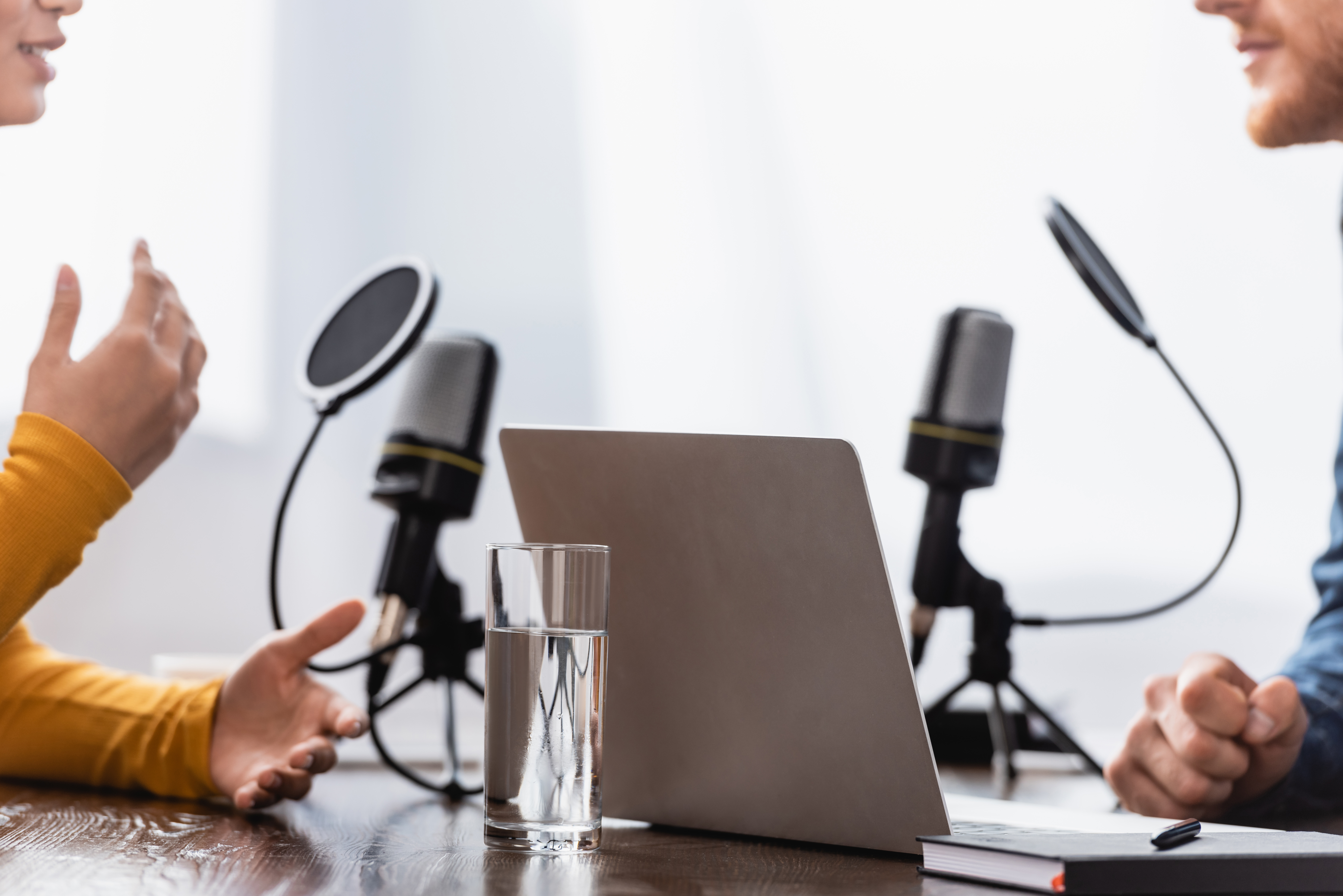Two people in conversation at a podcast recording desk with studio microphones